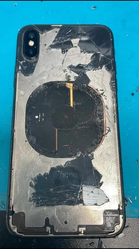 An iPhone with badly shattered back glass, waiting for repair on the bench.