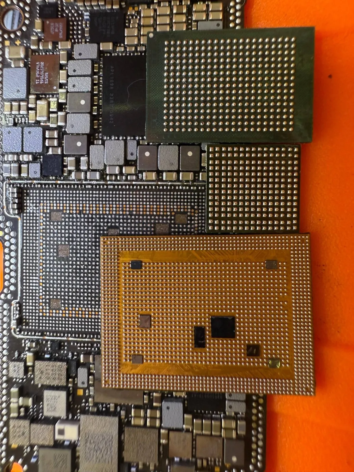 Chips removed from an iPhone main board, lying beside their empty pads on the repair mat.